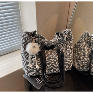 Detail of tweed tote bag with metal chain handles and fuzzy doll charm in natural light