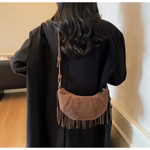 Brown suede half-moon bag with fringe tassels and knotted strap detail worn on black coat