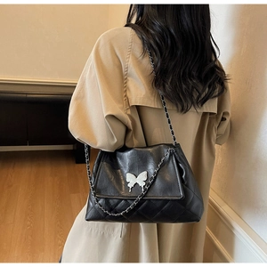 Vue arrière du mannequin portant un sac matelassé noir avec boucle papillon argentée