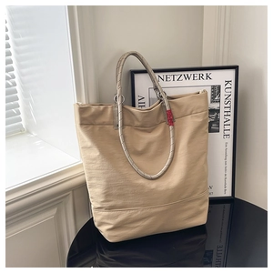 Detailed shot of beige tote bag featuring braided rope handles and red brand tag