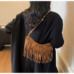 Detail of a brown suede crescent bag featuring long fringes and a knotted strap shoulder view