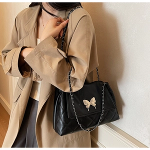 Détail d'un sac bandoulière matelassé noir avec boucle papillon argentée sur manteau