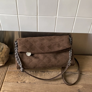 Detail view of dark brown suede shoulder bag with quilted diamond stitching and metal chain