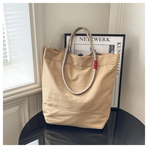 Close-up of a large khaki tote bag featuring woven rope handles and a red decorative tag