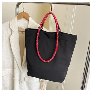 Detailed close-up of a black tote bag featuring colorful woven rope handles and metal rings
