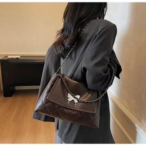 Détail d'un sac à bandoulière matelassé marron avec décoration papillon en métal argenté
