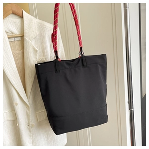 Detail of a large black tote bag featuring distinctive red and yellow rope shoulder straps