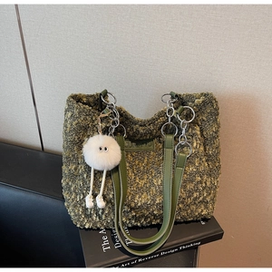 Detail of moss green bouclé tote bag with silver chain and monster plush charm accessory