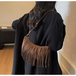 Detail of a brown suede crescent hobo bag with long fringes and boho knotted strap