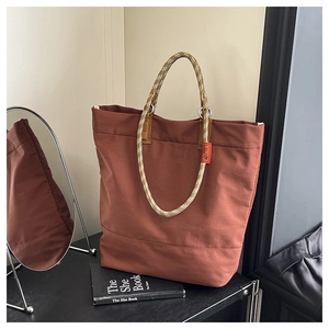 Detail view of brick red canvas tote bag with woven rope handles on a black wooden shelf