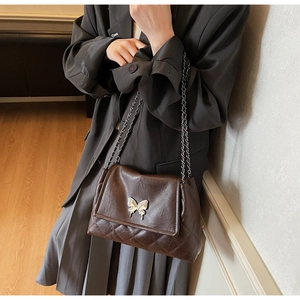 Détail du sac bandoulière en cuir marron foncé avec fermoir papillon et bandoulière chaîne
