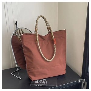 Detail of brick red tote bag with rope handles and silver metal rings on wooden table