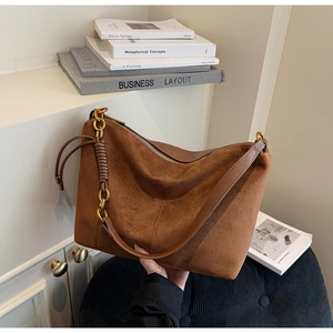 Detailed view of brown suede shoulder bag with woven chain strap and golden hardware