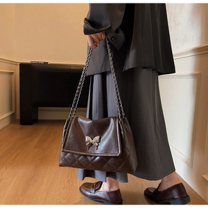 Détail du sac en cuir matelassé marron foncé avec chaîne argentée et boucle papillon