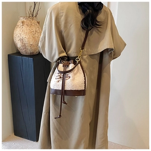Detail of plush bucket bag with brown leather trim and cursive embroidery on cream fleece