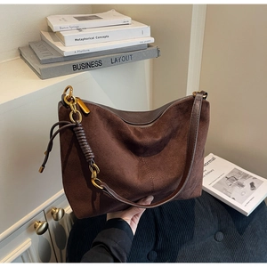 Detail view of dark brown suede handbag with leather stitching and gold hardware
