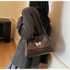 Modèle portant un sac bandoulière en cuir marron foncé avec fermoir papillon argenté