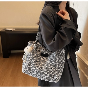 Close-up of black and white tweed crossbody bag with chain strap and plush pendant