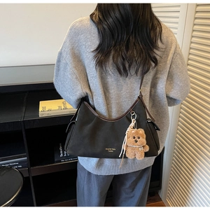Dettaglio borsa sottobraccio nera opaca con logo dorato e ciondolo orsetto di peluche