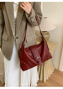 Detailed view of red retro leather hobo bag with metal buckle and silver rivets worn by model