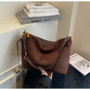 Detail of dark brown suede shoulder bag featuring contrast stitching and gold chain hardware