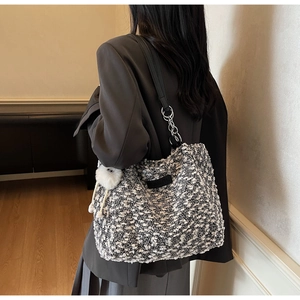 Detail of tweed tote bag featuring black leather straps and white faux fur pompom charm