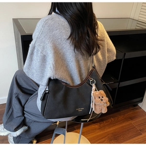 Dettaglio borsa a spalla in camoscio nero con finiture in pelle marrone e ciondolo orso