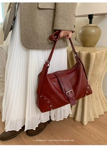 Deep red vintage tote bag with silver rivets held by model in retro setting
