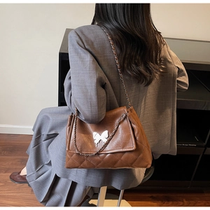Détail du sac matelassé marron à chaîne avec fermoir papillon blanc sur modèle