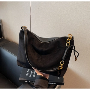 Detail of black suede hobo bag featuring gold chain and woven leather shoulder strap
