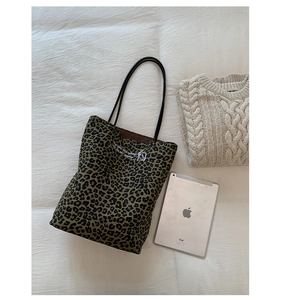 Flat lay of leopard print canvas tote bag with black handles on white fabric background