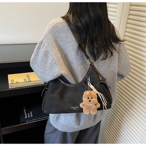 Dettaglio della borsa a spalla in camoscio nero con finiture in pelle marrone e orsetto