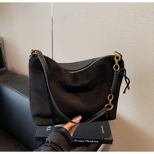 Detail of black suede and smooth leather shoulder bag featuring a gold chain and leather handle