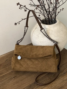 Quilted caramel suede shoulder bag with gold chain strap on a rustic wood surface