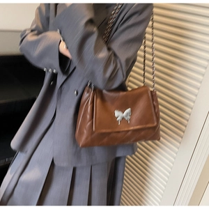 Sac bandoulière marron matelassé avec boucle papillon argentée porté par le mannequin