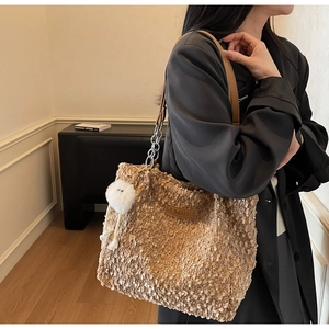 Detailed shot of brown fuzzy tote bag featuring a metal chain strap and white plush pompom