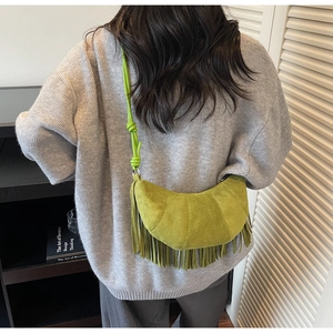 Close-up of vibrant green suede crescent bag featuring long tassels and knot shoulder strap