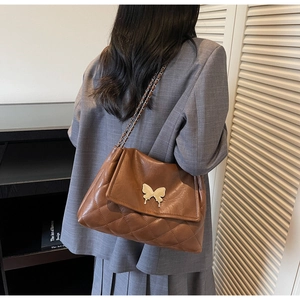 Détail du sac matelassé marron avec fermoir papillon doré et bandoulière en chaîne
