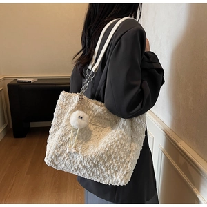 Detail of off-white plush tote bag with leather strap, metal chain, and cute doll pendant