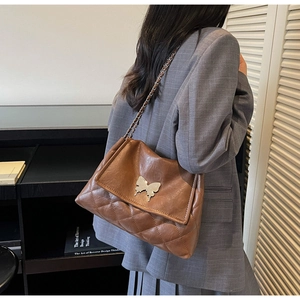 Détail d'un sac porté épaule marron matelassé avec boucle papillon argentée et chaîne