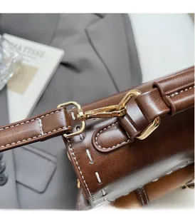 Dettaglio dello zaino in pelle marrone vintage con fibbie dorate e cuciture bianche a vista