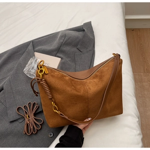 Macro detail of dark brown suede shoulder bag with gold chain and leather woven strap