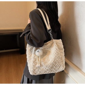 Detailed view of white faux fur tote bag with plush charm and chain strap worn by model