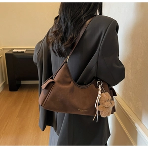 Dettaglio della borsa tote in pelle scamosciata marrone scuro con tracolla e ciondolo a orso