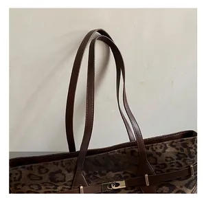 Detailed close-up of leopard print tote bag with brown leather handles and gold metal buckles