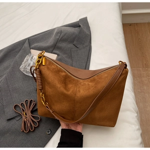 Detail of caramel suede tote bag featuring stitching and gold chain strap on grey blazer