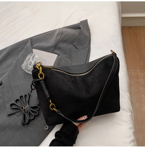 Detail of black faux suede shoulder bag with gold chain and detachable strap on blazer