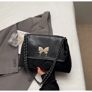 Détail du sac bandoulière noir matelassé avec boucle papillon en métal et bandoulière chaîne
