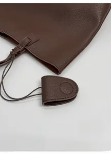 Detail of dark brown lychee grain leather bucket bag featuring elegant pendant and strap craft