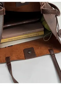 Detail view of large storage capacity showing laptop and books inside dark brown bucket bag